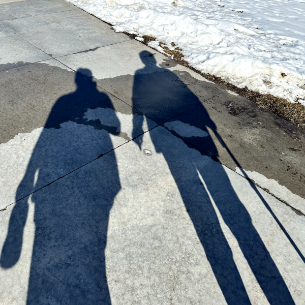 Shadows of Alyson and her mom on the concrete sidewalk, with now on the grass.