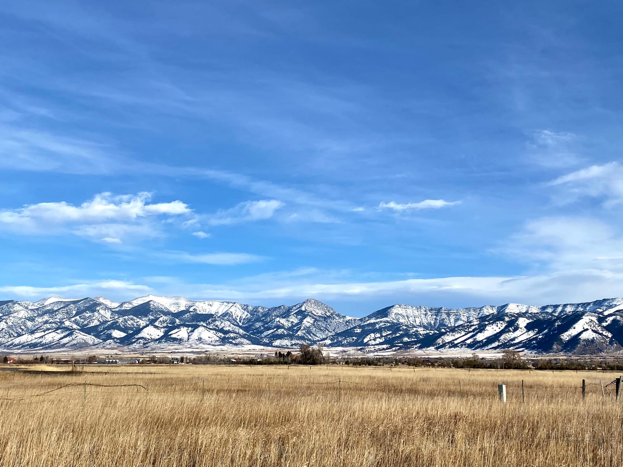 Photo of Bridger Mountains with blue skies, wispy clouds, brown fields, and snow on the mountains.