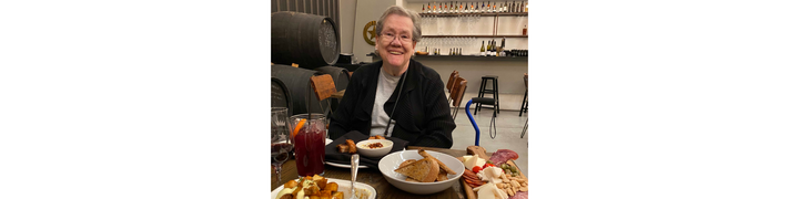 Alyson's mom smiling at the camera, with a variety of dishes before her at a restaurant.